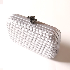 Silver woven satin evening clutch bag with dark metal knot clasp on white background