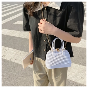 Detail of white shell-shaped PVC bag with lattice texture and gold chain on street
