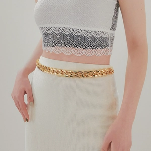 Detail of chunky gold chain waist belt with glossy finish on elegant white knit dress