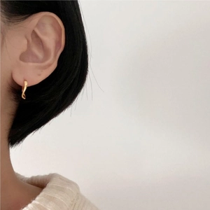 Close-up of minimalist gold curved hoop earring worn by a model against white background