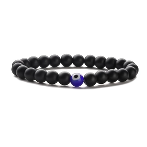 Elastic beaded bracelet with matte black beads and blue glass evil eye charm on white background