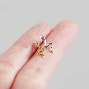 Makroaufnahme von minimalistischen Schlangen-Ohrsteckern in Gold und Silber auf Fingern