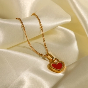 Détail d'un collier cœur doré vintage avec incrustation rouge sur tissu en soie beige