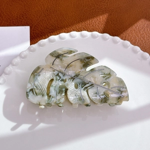 Close-up of monstera leaf acetate hair claw clip with marble texture on lace plate
