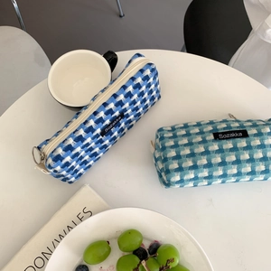 Détail des trousses tissées aux motifs à carreaux bleus et sarcelles sur table blanche