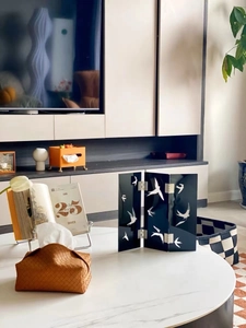 Brown woven leather tissue box and black swallow screen decor on a modern coffee table