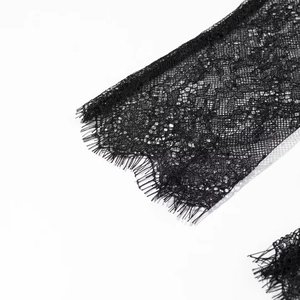 Détail du tissu en dentelle noire avec motifs floraux et bordures à franges délicates