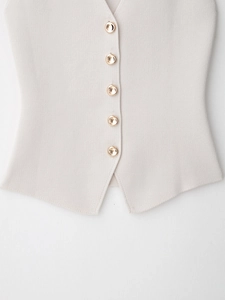 Detail of beige knitted vest featuring five metallic gold buttons and V-cut hemline
