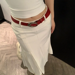 Détail d'une ceinture en cuir rouge croco avec boucle ovale argentée sur une jupe blanche