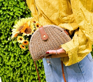 Detail of semi-circular straw crossbody bag with brown leather clasp and thin strap