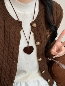 Detailed view of a brown velvet heart pendant on a cable-knit sweater with gold buttons