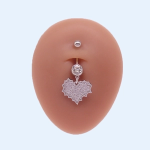 Détail d'un piercing de nombril en acier argenté avec un pendentif en forme de cœur brillant
