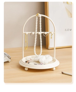 Arched beige metal jewelry rack with hooks and base tray on a wooden table