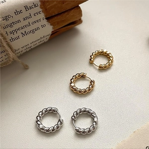 Close-up of vintage twisted rope hoop earrings in gold and silver finish on a textured base