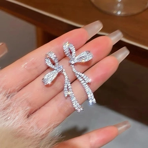 Vue détaillée de boucles d'oreilles nœud argentées avec pompons et finition brillante