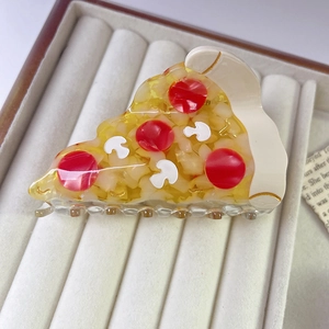 Detailed view of an acrylic pizza hair claw clip resting on a beige velvet jewelry tray