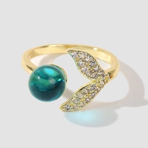 Close-up of golden mermaid tail ring with green crystal bead and pavé set rhinestones
