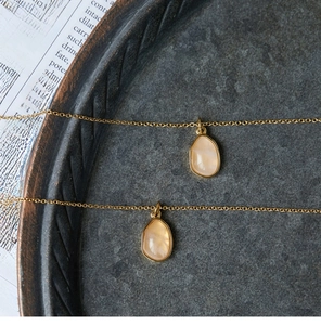 Detail of two 18K gold plated titanium necklaces with water-drop orange stone pendants