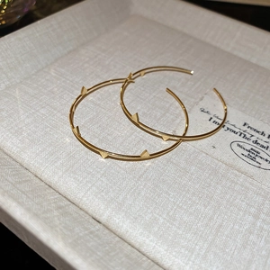 Detail of golden hoop earrings with studded triangle accents on a jewelry display tray