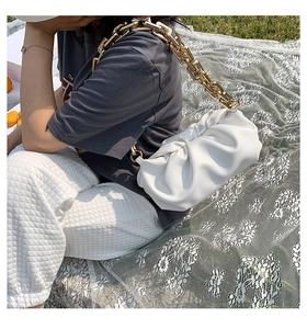 Detail of white pleated cloud bag with chunky gold chain strap on a picnic grass setting