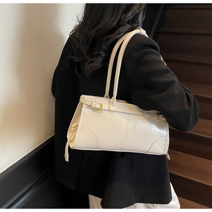 Detail view of a cream leather shoulder bag with gold hardware worn over a dark suit blazer