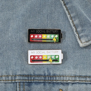 Detail of sliding social battery enamel pin on blue denim fabric background