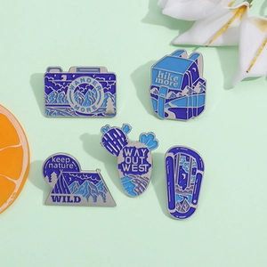 5-piece outdoor travel enamel pins set featuring camera cactus and backpack on green background