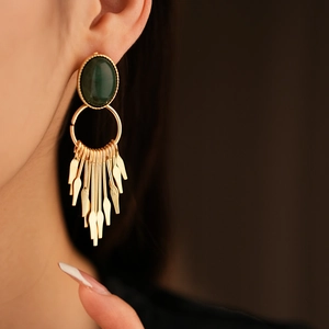 Macro detail of gold tassel earrings with dark green oval gemstone on model
