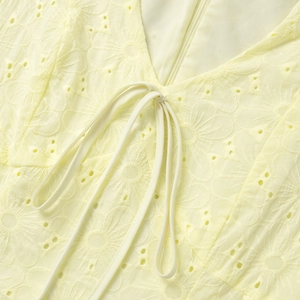 Detail of yellow cotton dress showing delicate floral eyelet embroidery and V-neck tie