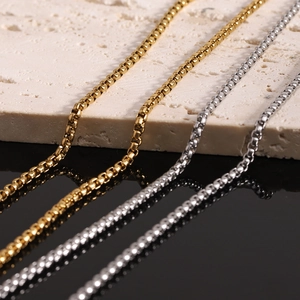 Detail of two-tone gold and silver box chains on a textured beige stone surface