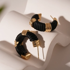 Détail de boucles d'oreilles créoles C en tissu noir et métal doré sur socle blanc