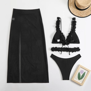 Detailed flat lay of three-piece black bikini set with ruffle edges and sheer mesh maxi skirt