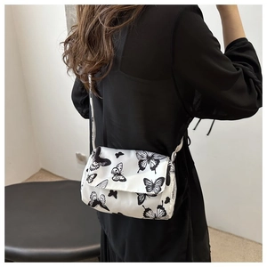 Detail view of a white crossbody bag with butterfly prints worn by a model in a casual setting