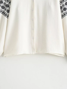 Detail of white blouse featuring black ethnic embroidery on long sleeves and buttons