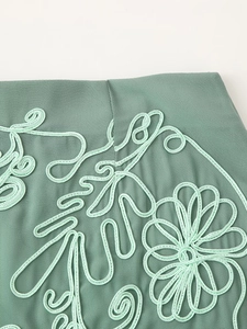 Détail du tissu vert sauge avec broderie florale vert menthe et textures raffinées
