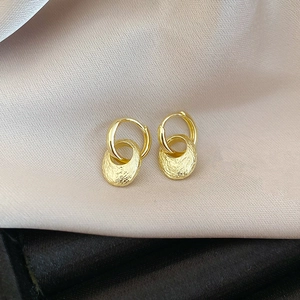 Detail of gold oval drop earrings with brushed metal texture on silk background