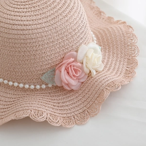 Pink wide-brim straw hat featuring satin roses, pearl band, and wavy lace edge for sun protection