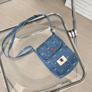 Detail van blauwe denim schoudertas met sterborduurwerk en kattenlabel op stoel