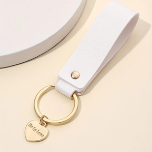 Close-up of white leather strap with gold heart pendant engraved with He is love