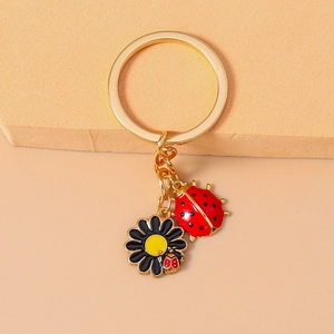 Close-up of golden keychain with red enamel ladybug and black daisy flower pendant