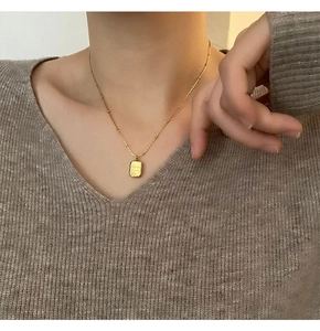 Close-up of gold rectangular pendant necklace with bead chain on model's neck