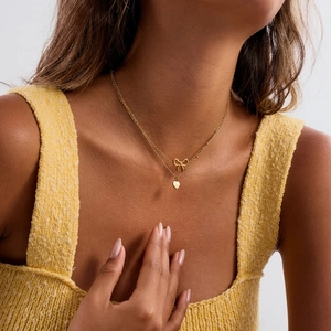 Detail of layered gold stainless steel necklace with bow and heart pendants on a model