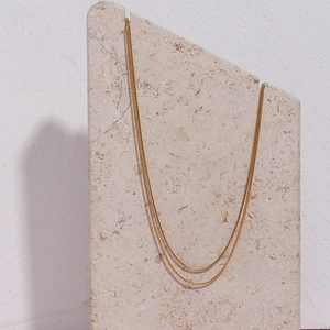 Detail of minimalist 18K gold plated double layer snake chain necklace on stone base