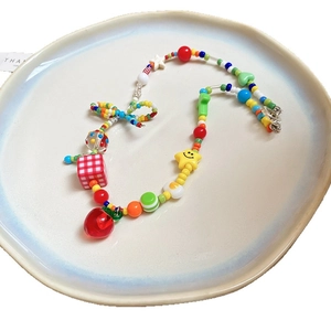 Colorful beaded necklace with cherry, star and heart charms on a beige ceramic plate