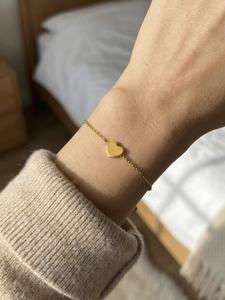Detail of a minimalist gold heart pendant bracelet worn over a beige knit sweater
