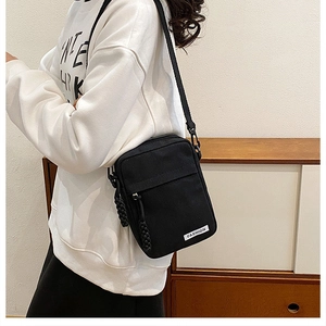 Detail of black canvas crossbody bag featuring fashion label and braided zipper pull