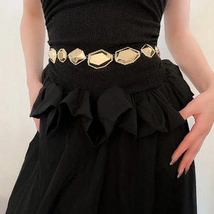 Ceinture métallique dorée à facettes géométriques portée sur une robe noire