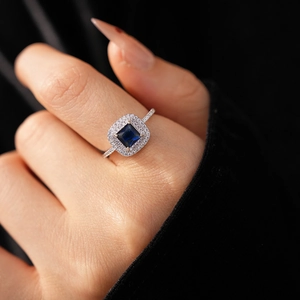 Detailed close-up of a square blue gemstone ring with zircon halo setting on finger