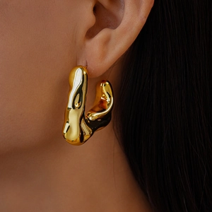 Close-up of golden irregular wavy earring with polished liquid metal finish on model