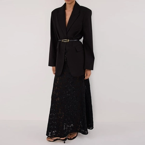 Detail shot of sheer black lace maxi skirt paired with a belted blazer on white background